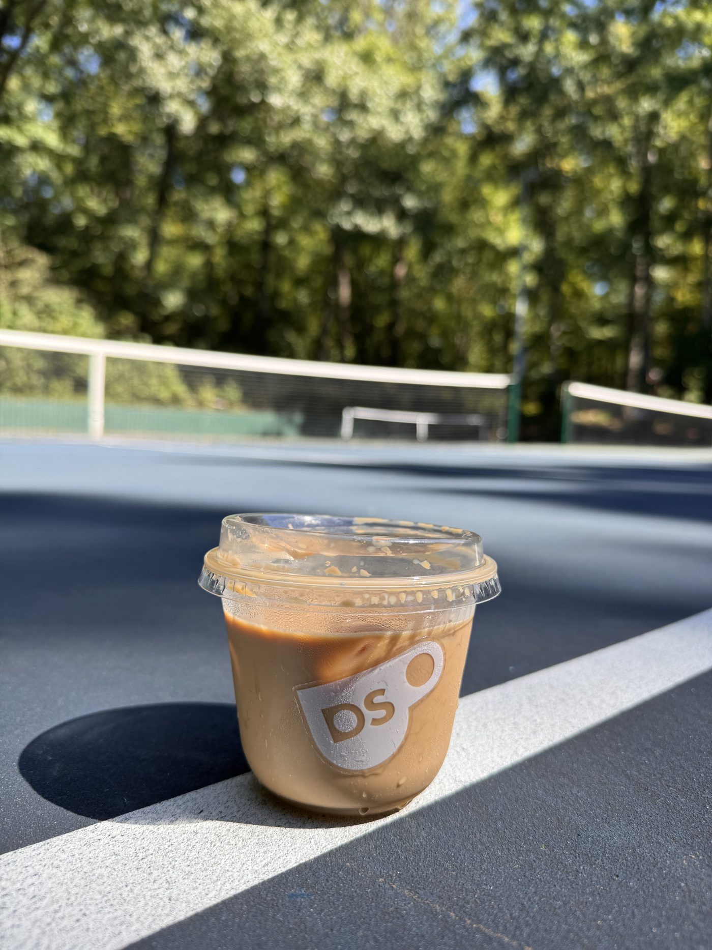 Iced latte in a Drop Shot branded cup served courtside at a Northern Virginia tennis club